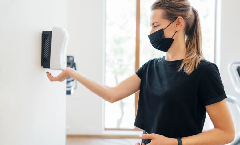 side-view-woman-with-medical-mask-disinfecting-her-hands-gym_23-2148762656